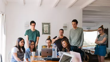 Grupo de personas trabajando en equipo alrededor de una mesa con laptops.