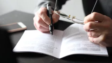 Persona leyendo un documento con gafas y bolígrafo en mano.