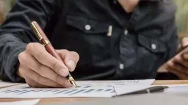 Persona revisando gráficos con un bolígrafo y un teléfono móvil.