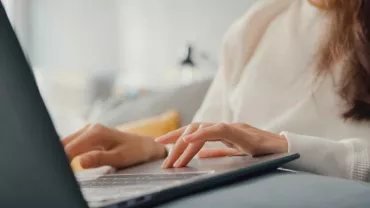 Mujer trabajando en una laptop en un sofá.