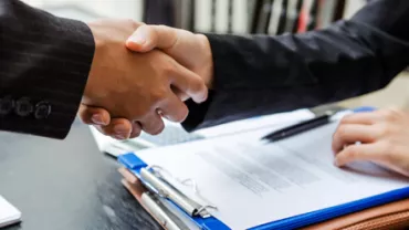 Dos personas se dan la mano frente a documentos.