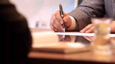 Persona firmando un documento en una reunión de negocios.